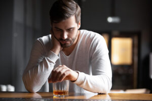 A man drinks an alcoholic beverage to cope with his emotions, an example of what self-medicating looks like.